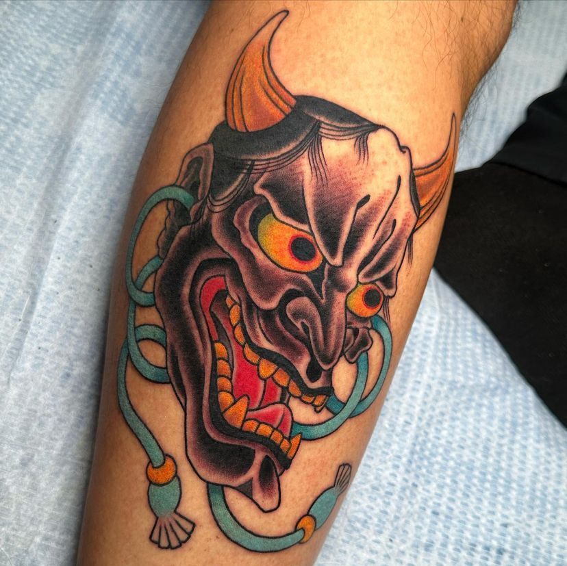 Colorful horned demon tattoo on an arm, with sharp teeth and glowing eyes