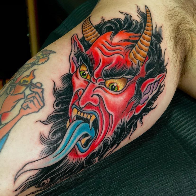 Red oni tattoo on a bent arm, with horns, yellow eyes, and a blue tongue
