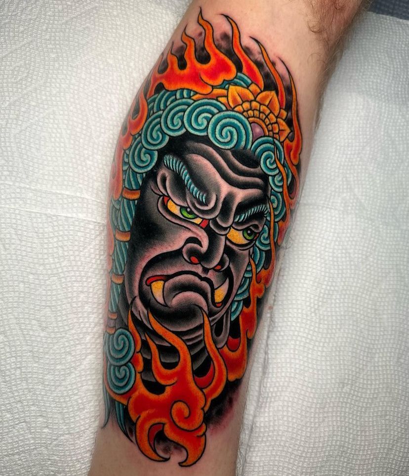 Colorful Japanese-style demon tattoo with teal hair, red flames, and a fierce expression on a forearm
