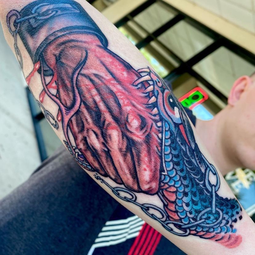Close-up of a colorful forearm tattoo with blue, red, and black koi or fish scales
