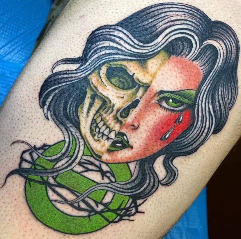 Colorful tattoo of a half-skull, half-woman face with black hair and a green snake below