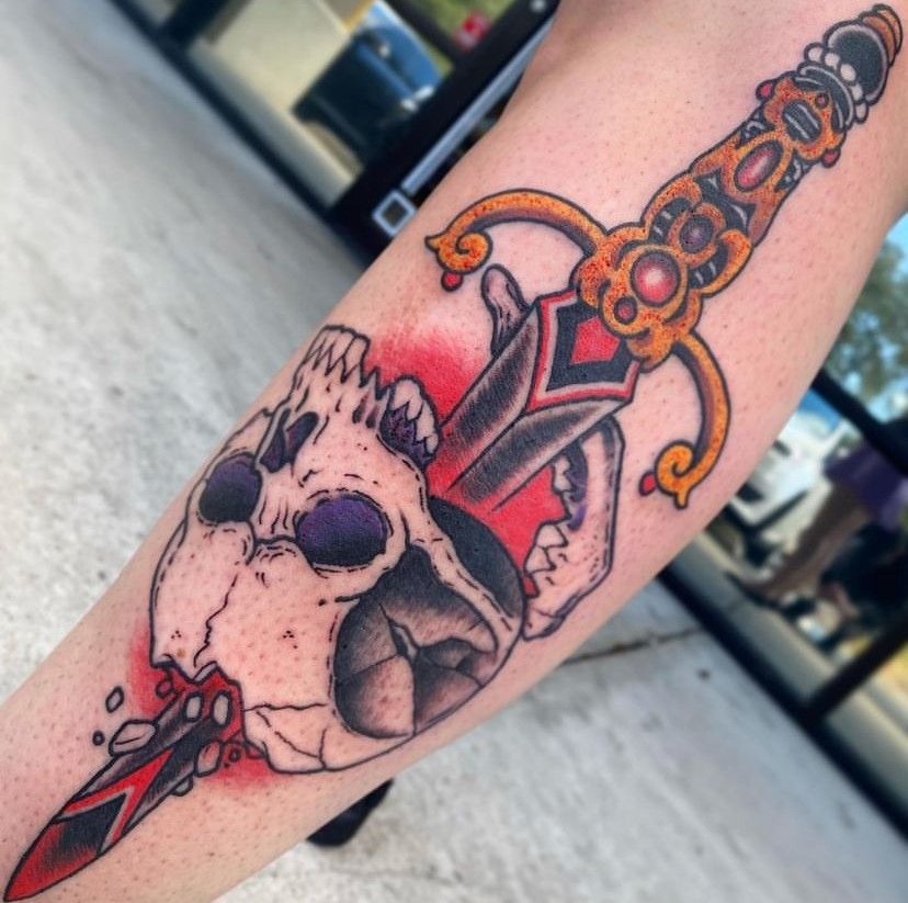 Skull tattoo on a forearm with a red dagger piercing through it, in a tattoo studio