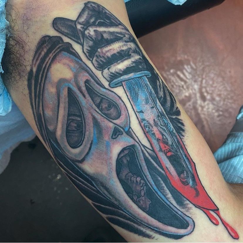 Close-up of a colorful horror-style Ghostface tattoo with a knife and red blood drips on skin