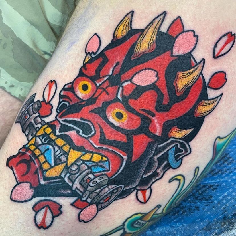 Red and black oni-style tattoo with horns, yellow eyes, and pink petal-like accents on skin