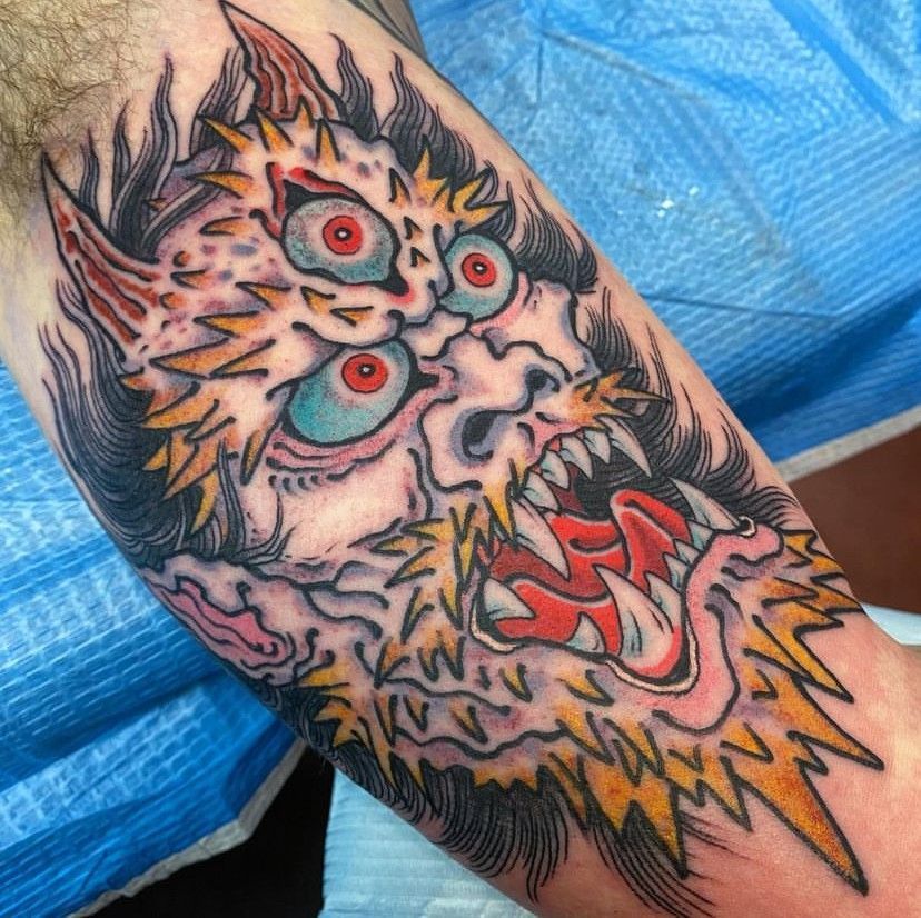 Colorful tattoo of a fierce creature with red eyes and sharp teeth on an arm