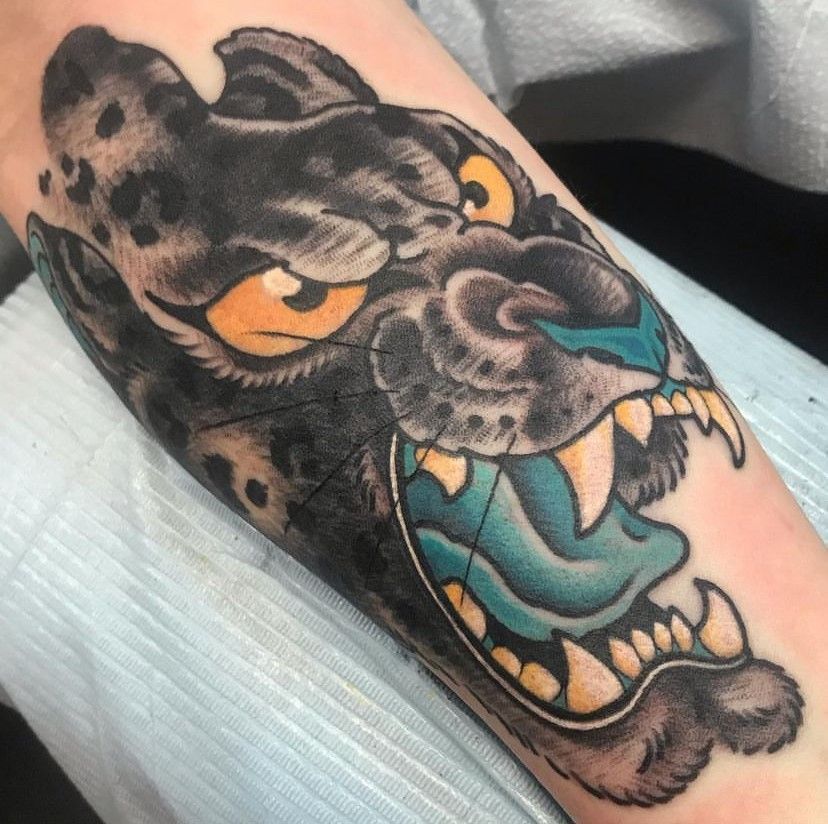 Color tattoo of a snarling black panther with yellow eyes and teal mouth on an arm