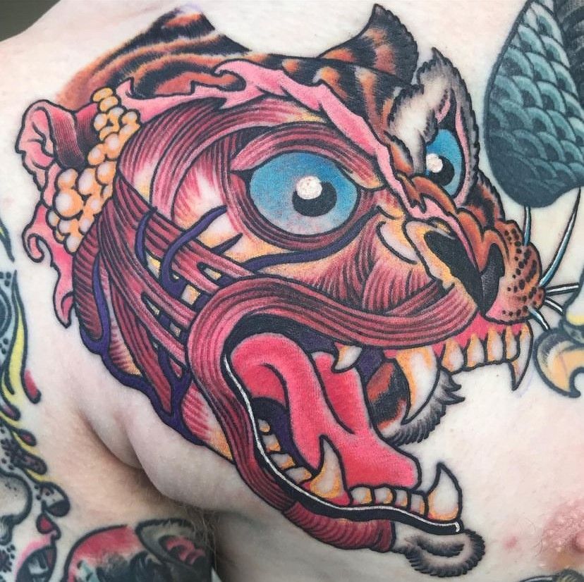 Colorful tattoo of a snarling owl with blue eyes, pink tongue, and orange-black feathers on skin