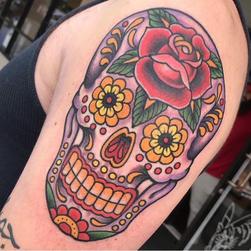 Colorful sugar skull tattoo with pink rose and yellow flowers on an upper arm