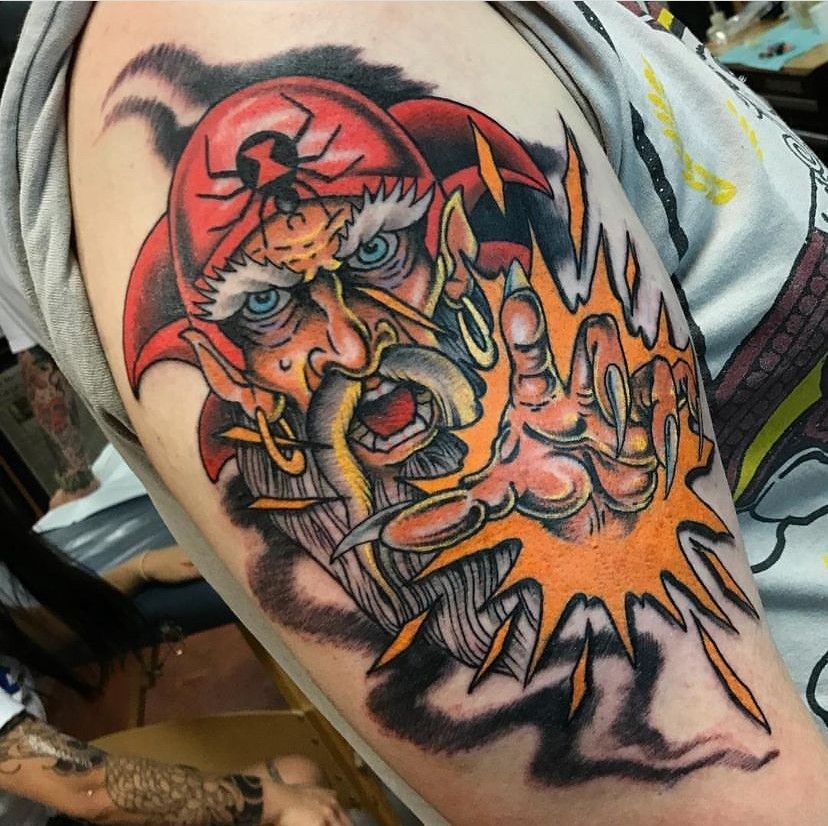 Colorful tattoo of a snarling bearded face with red headscarf and orange burst on skin