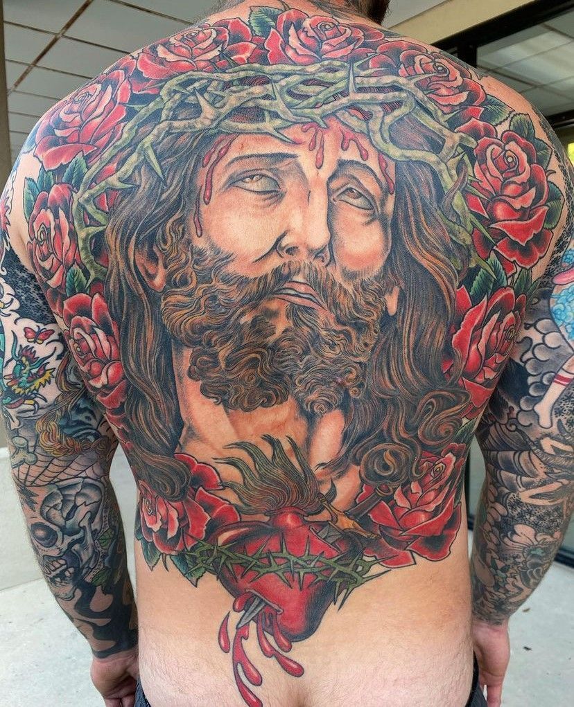 A person’s back covered in a large colorful tattoo of a bearded face with roses around it.