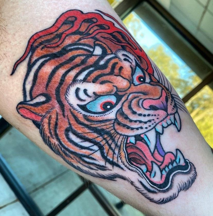 Colorful tiger head tattoo on skin, snarling with orange, black, and red details