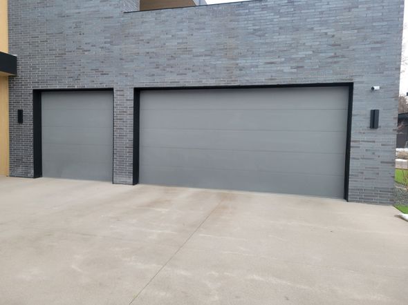 A gray stone exterior wall features two modern, light gray sectional garage doors set against a concrete driveway.
