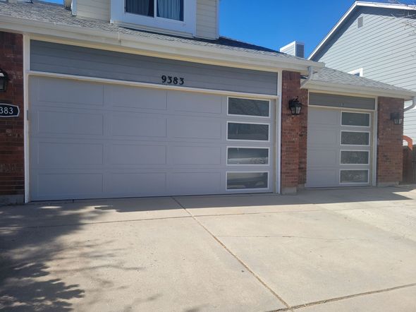 A suburban home exterior featuring two gray garage doors with vertical windows, set against a brick and siding facade.