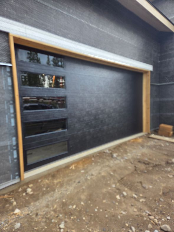 Modern dark gray garage door with a vertical row of five rectangular windows on the left side, set in a new construction.