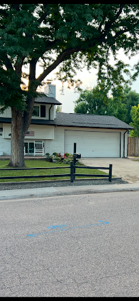 A white house with a garage and a large tree in the front yard, separated from the street by a black wooden fence.