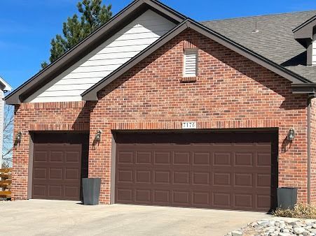 A brick suburban house exterior featuring a large two-car garage door and a smaller single-car garage door in brown.