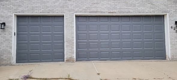 Two dark gray garage doors with a rectangular paneled design set in a light-colored brick wall.