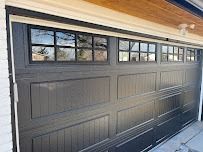 Dark gray garage door with windows featuring a grid pattern, installed under a wooden soffit.