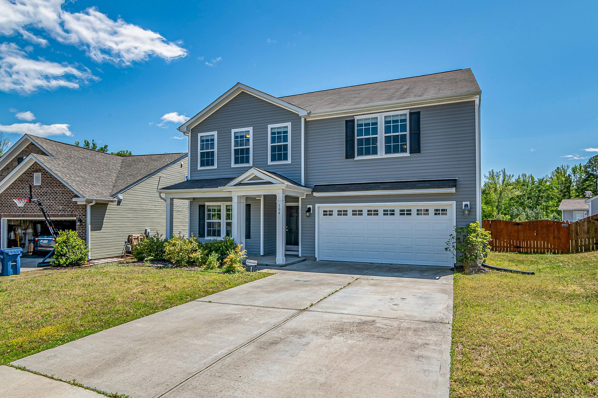 Two-story gray suburban house with white garage and driveway under a blue sky