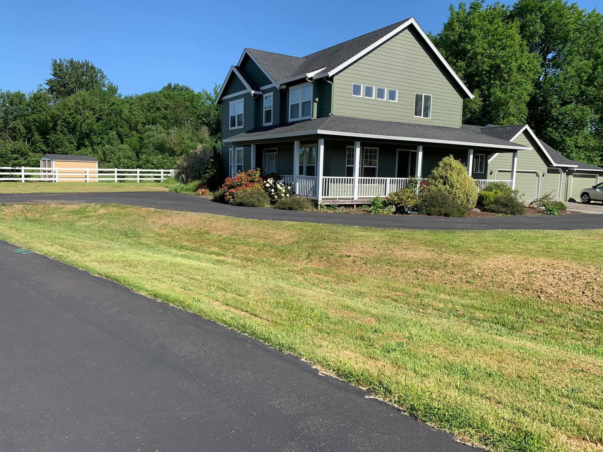 A large green house with a porch is sitting on top of a lush green field.