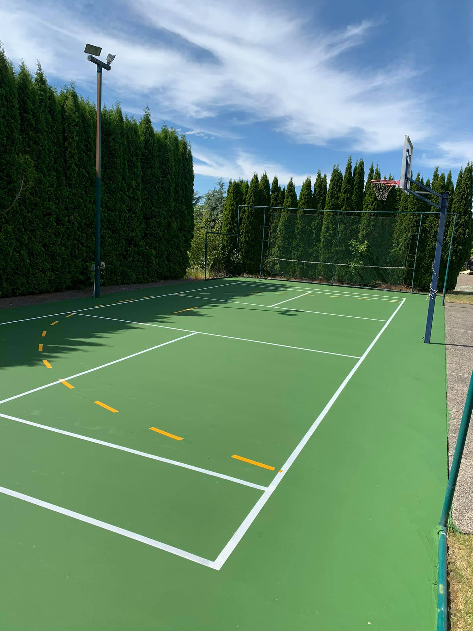 A green tennis court with white lines and trees in the background.