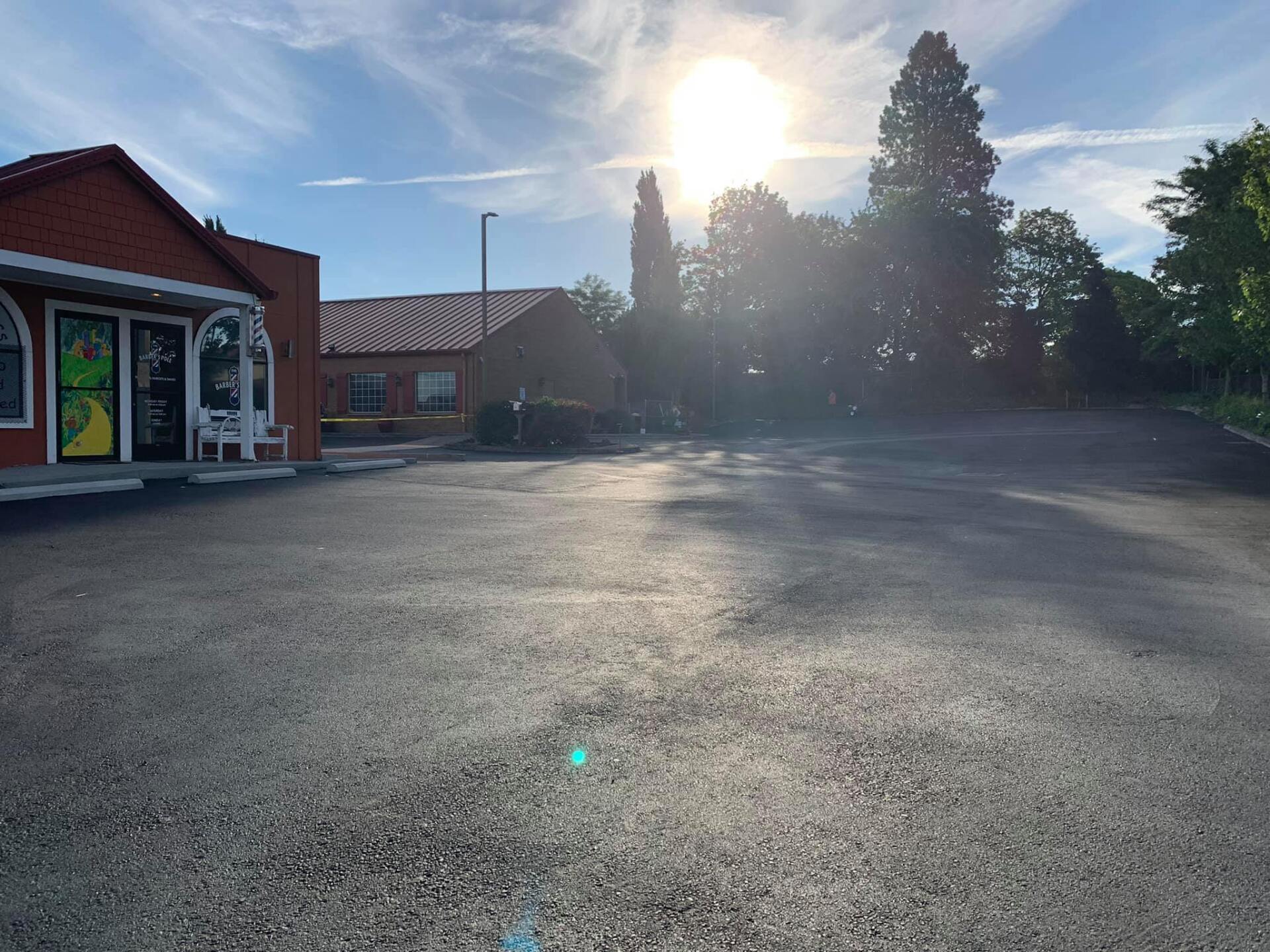 A parking lot in front of a building with the sun shining through the trees