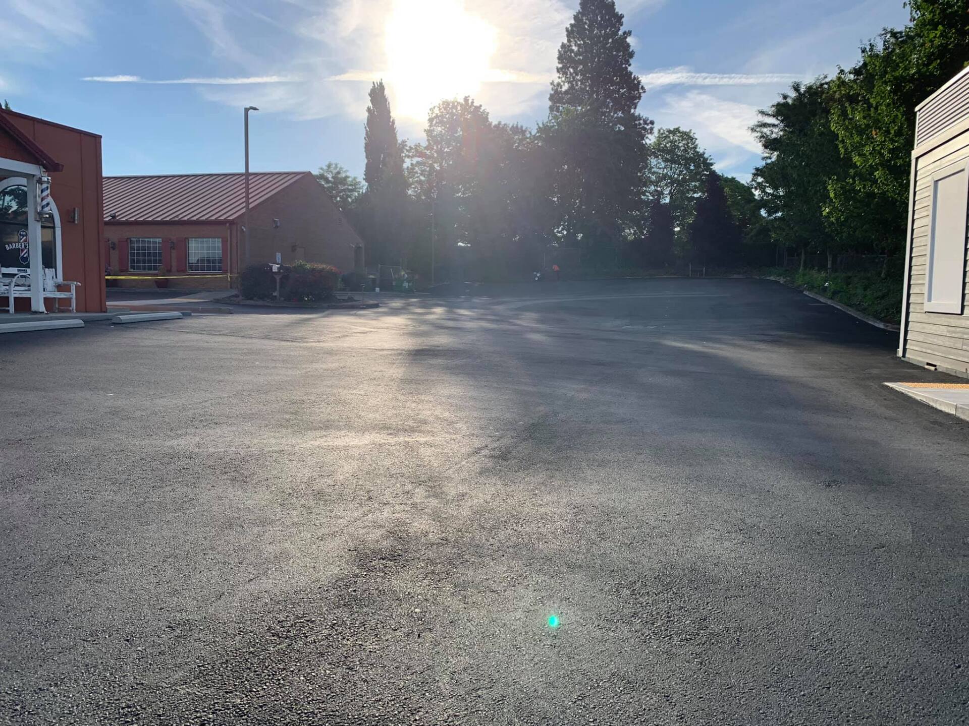 A parking lot with a building in the background and the sun shining through the trees.