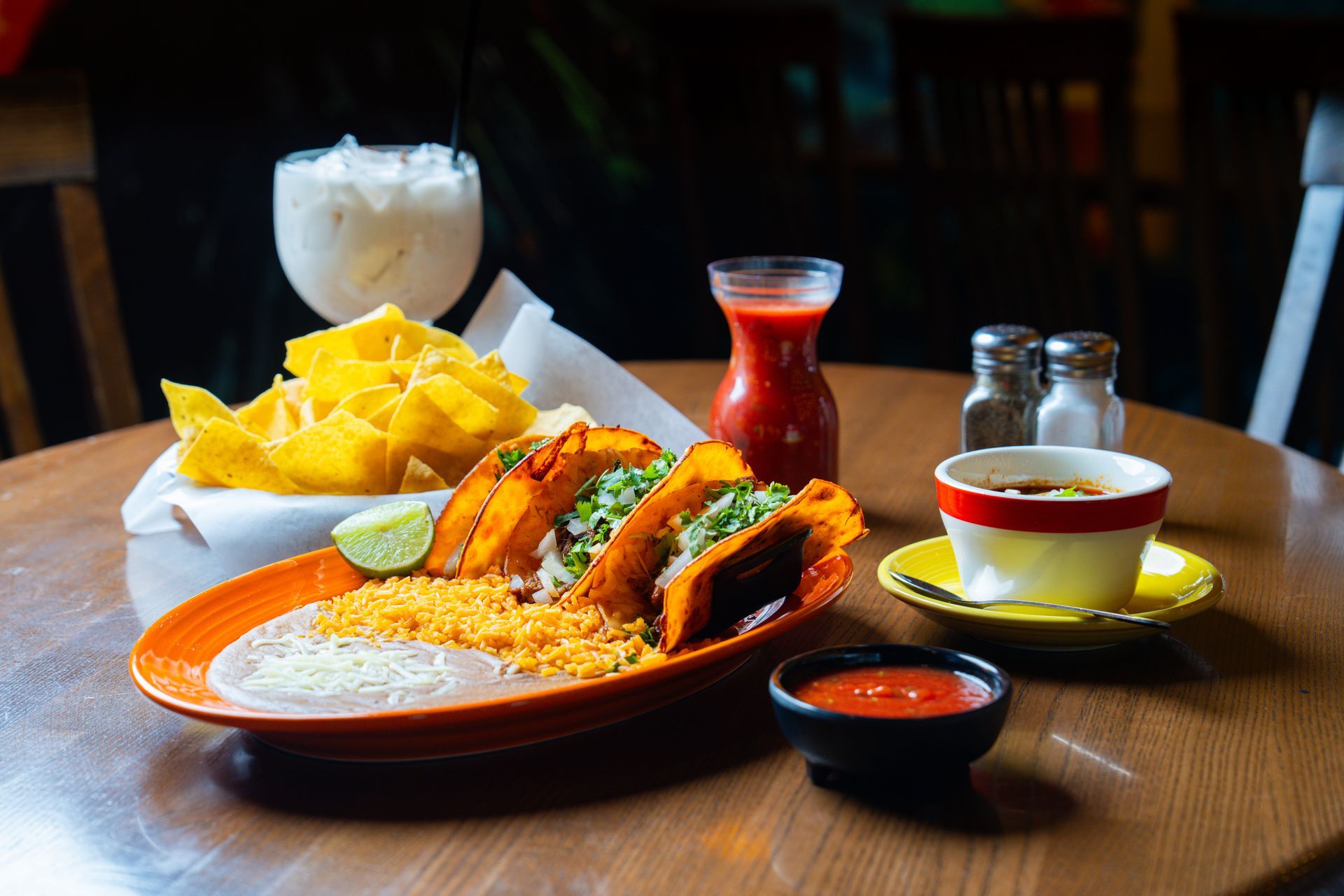 Two people smiling and holding drinks with straws at an outdoor table with a vibrant, blurred background.