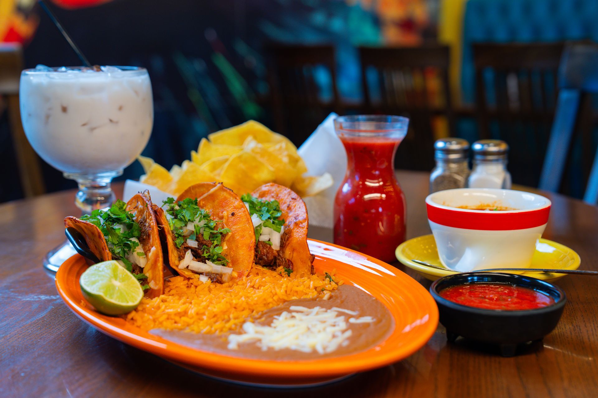 Restaurant interior featuring a large mural of a person in a decorative hat, wooden ceiling beams with lights, and tables.