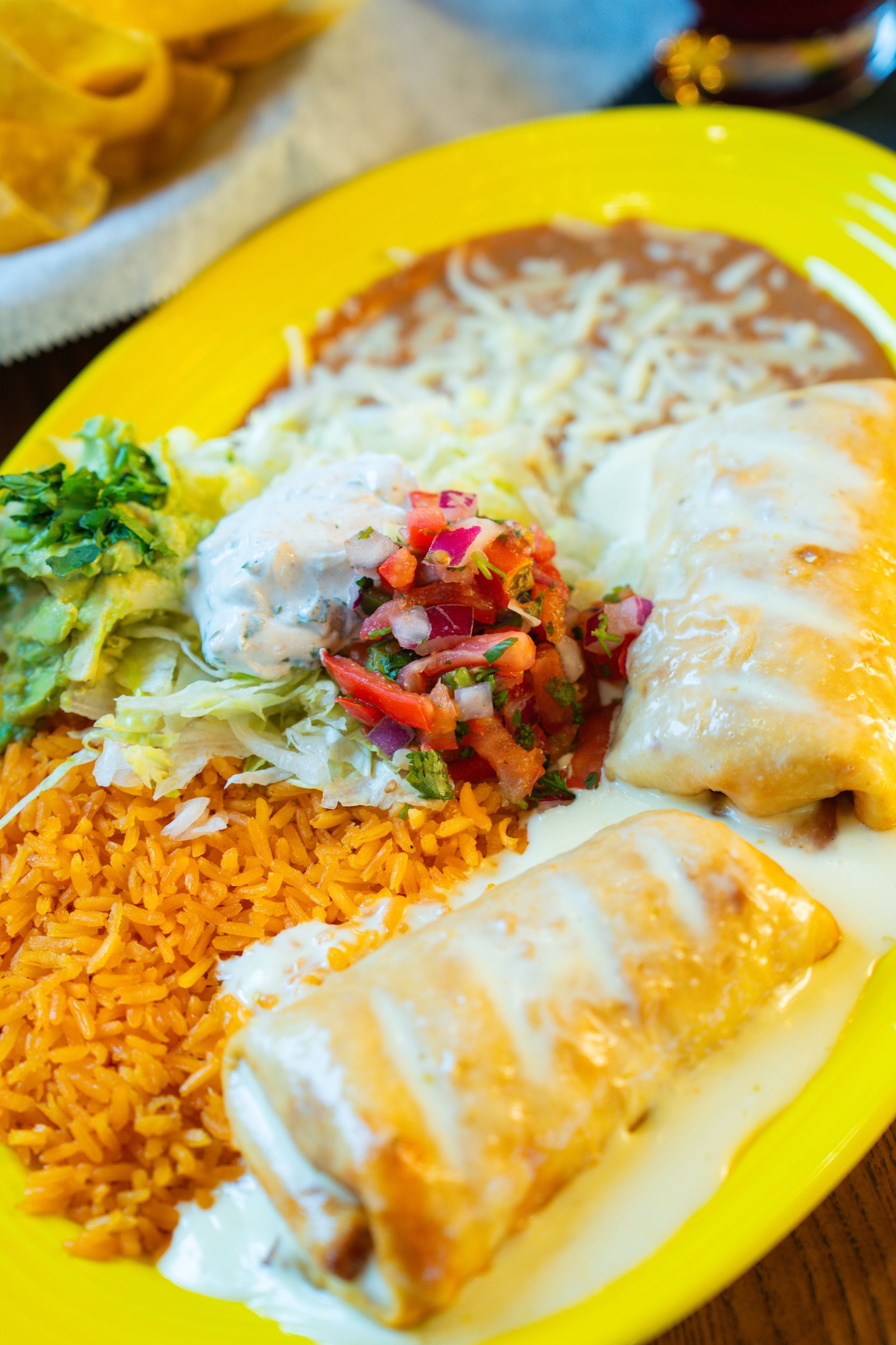 A tray of four assorted tacos with a side of green and red salsa, garnished with lime wedges on branded paper.