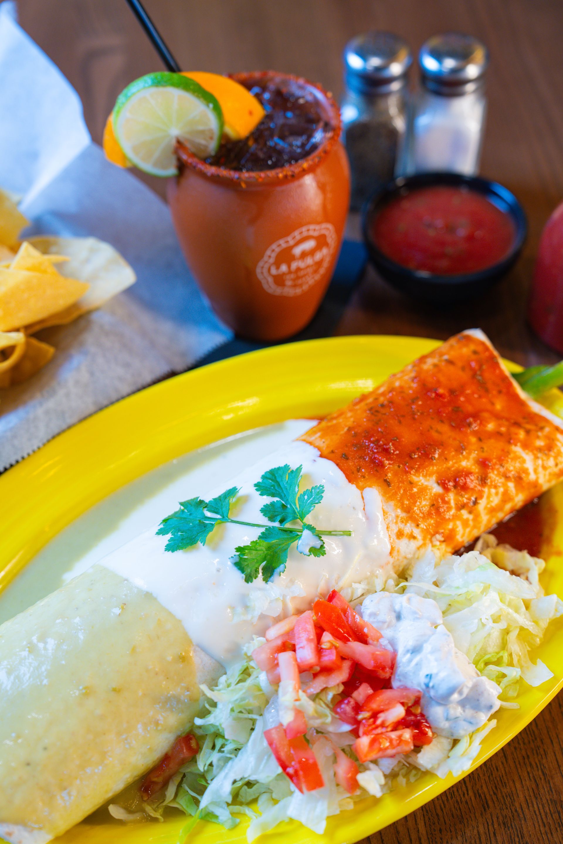 A breakfast burrito filled with meat and eggs, topped with salsa, served with guacamole and sliced avocado on a plate.