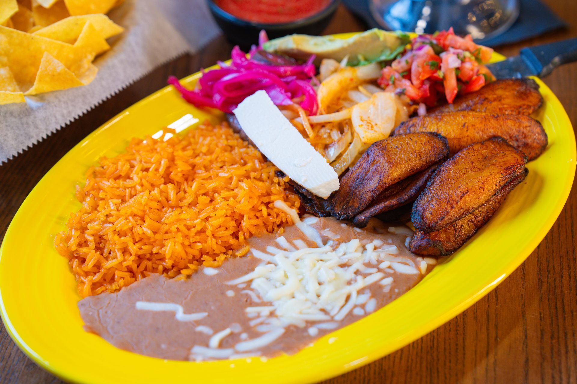 A margarita with a pineapple garnish and a chili-rimmed glass, next to a plate of enchiladas on a red plate.