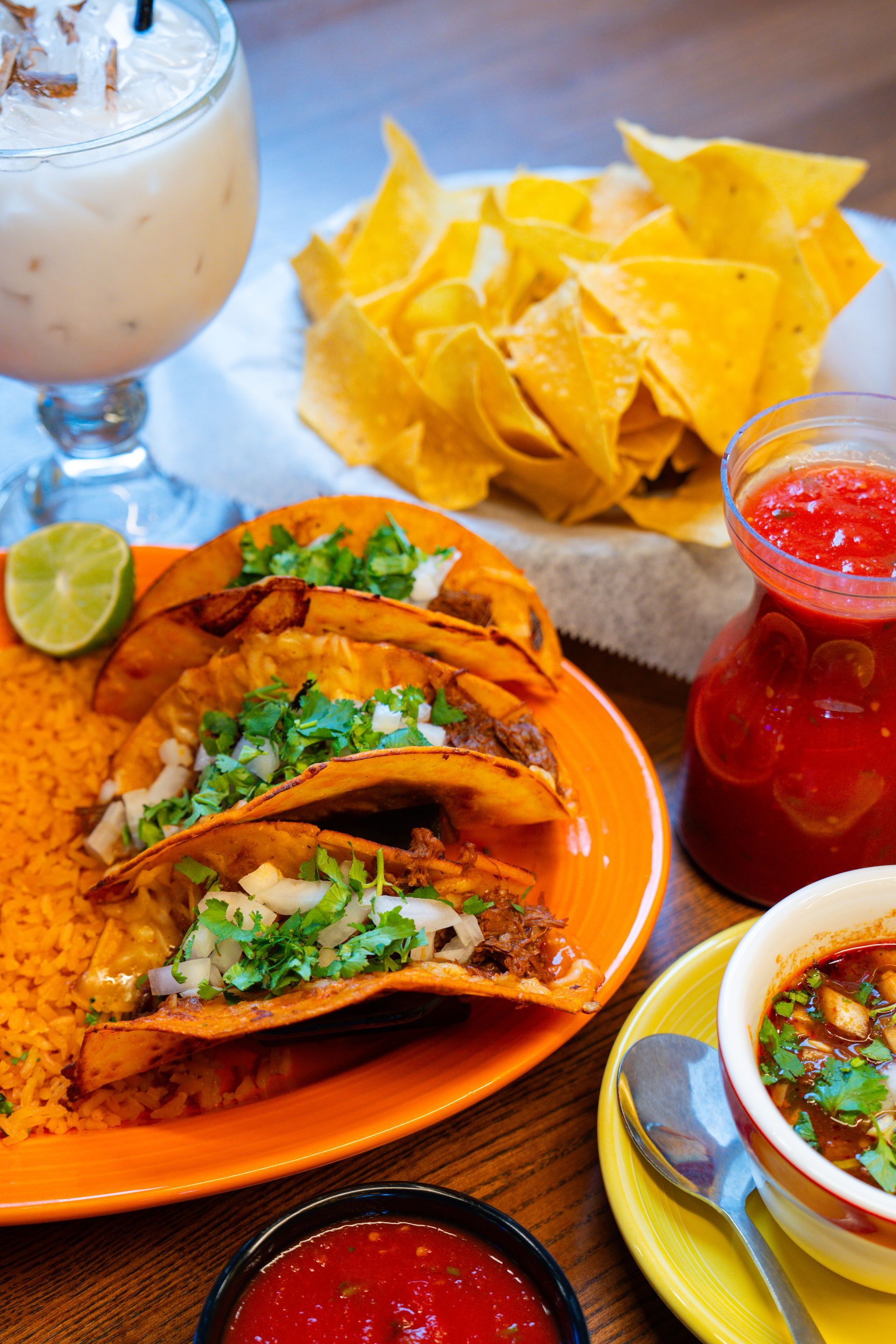 A steaming cast-iron skillet of steak fajitas sits on a table with other Mexican dishes and a margarita in the background.