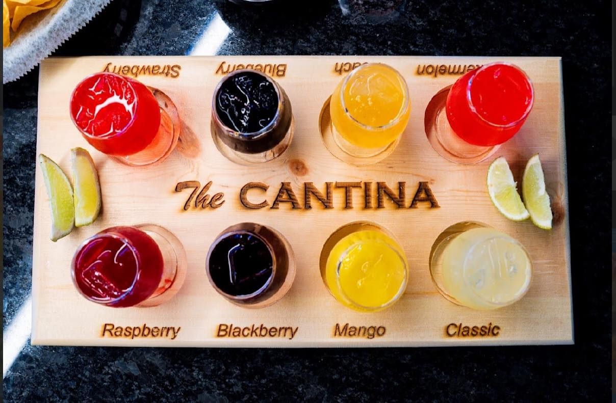 A smiling person holding a taco at a table with friends, with dishes and drinks in an outdoor dining setting.