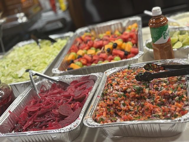 A colorful salad with sliced tomatoes, avocado, corn, diced red peppers, cilantro, and red onion rings in a pottery bowl.
