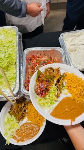 Interior of a restaurant with a bar featuring colorful stools, wood tables, and woven pendant lights under a black ceiling.