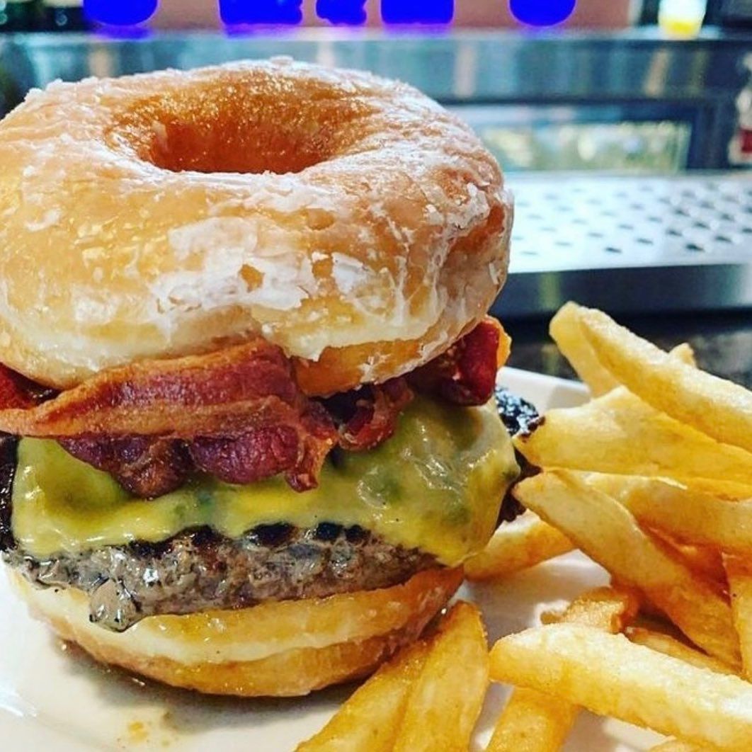 A donut shaped hamburger with cheese bacon and french fries on a plate