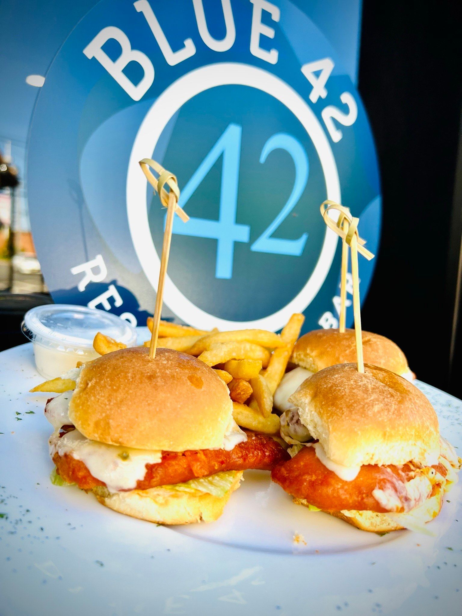 Two chicken sliders and french fries on a plate in front of a blue 42 restaurant logo.