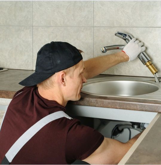 Plumber working on faucet installation beneath kitchen sink. Plumber installing or repairing a kitchen sink faucet under the countertop.
