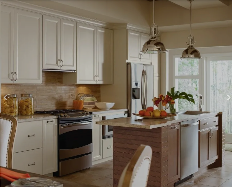 Ultracraft – Custom Cabinets Designed for Life Warm contemporary kitchen featuring Ultracraft cabinetry with white wall cabinets, contrasting wood island, stainless steel appliances, pendant lighting, and natural tile backsplash.