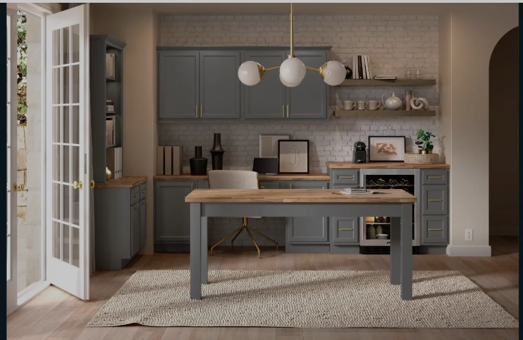Explore Stylish and Functional Cabinetry by Aristokraft Elegant home office featuring Aristokraft Cabinetry in soft gray, complemented by wood countertops, white brick accent wall, stylish modern chandelier, and abundant natural lighting.