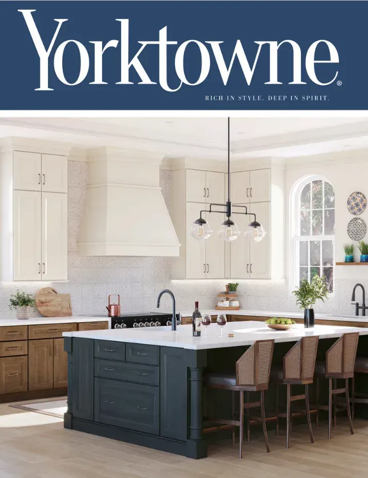 Explore Timeless Cabinetry Designs with Yorktowne Inviting kitchen featuring Yorktowne cabinetry with contrasting dark island, white upper cabinets, natural wood lower cabinets, elegant pendant lighting, and spacious seating area, showcasing modern elegance and warmth.