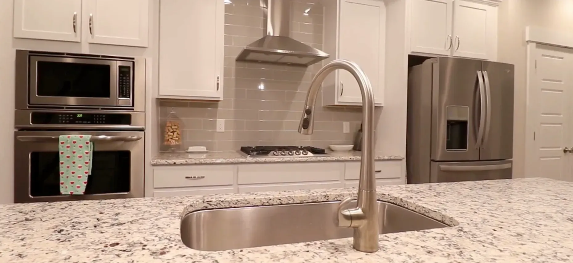 Discover Inspired Living paces with HOME by KBD Modern kitchen featuring stainless steel appliances, white cabinetry, subway tile backsplash, granite countertop, and a sleek pull-down faucet.