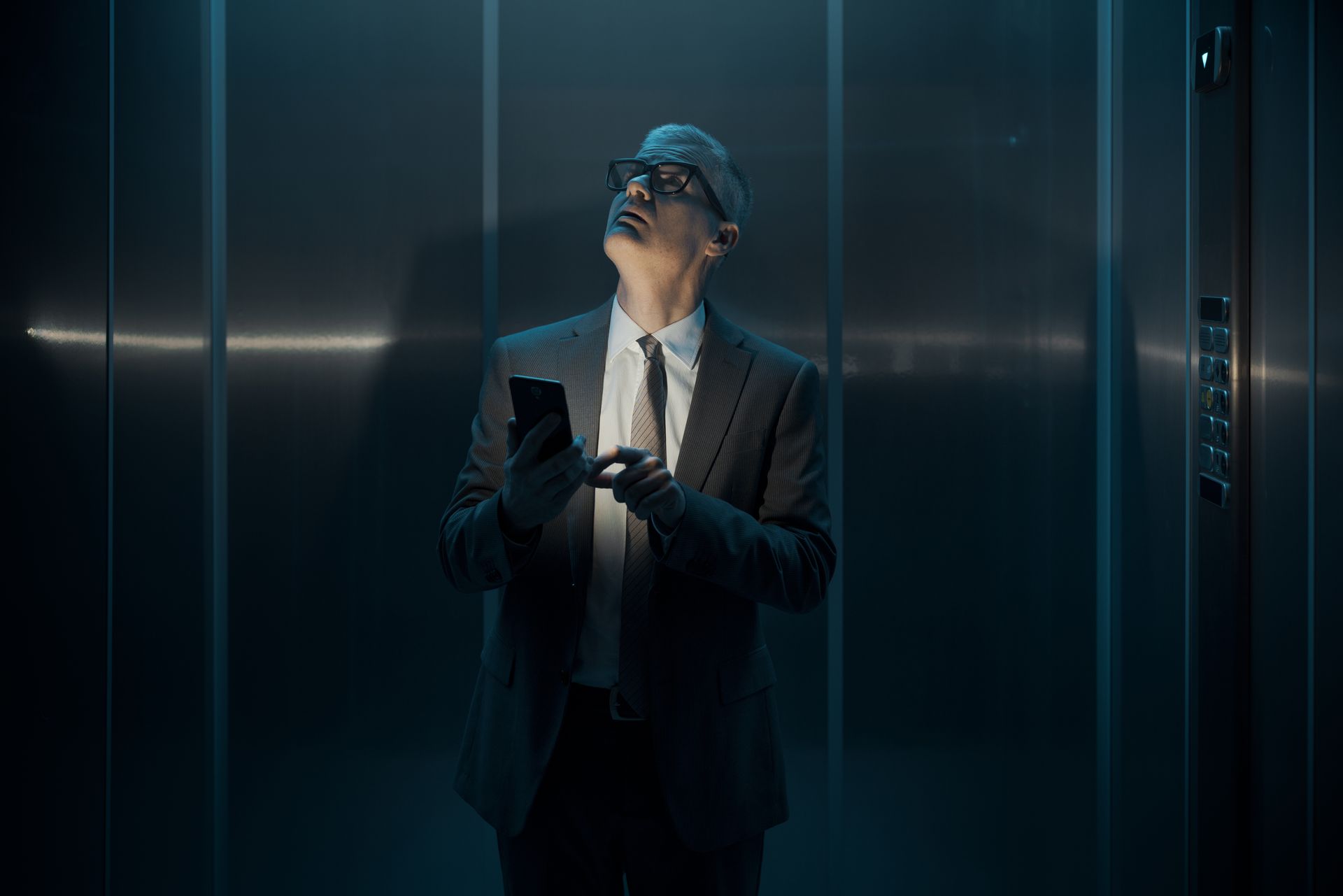 A businessperson wearing a suit, stuck inside a commercial elevator due to a power outage 