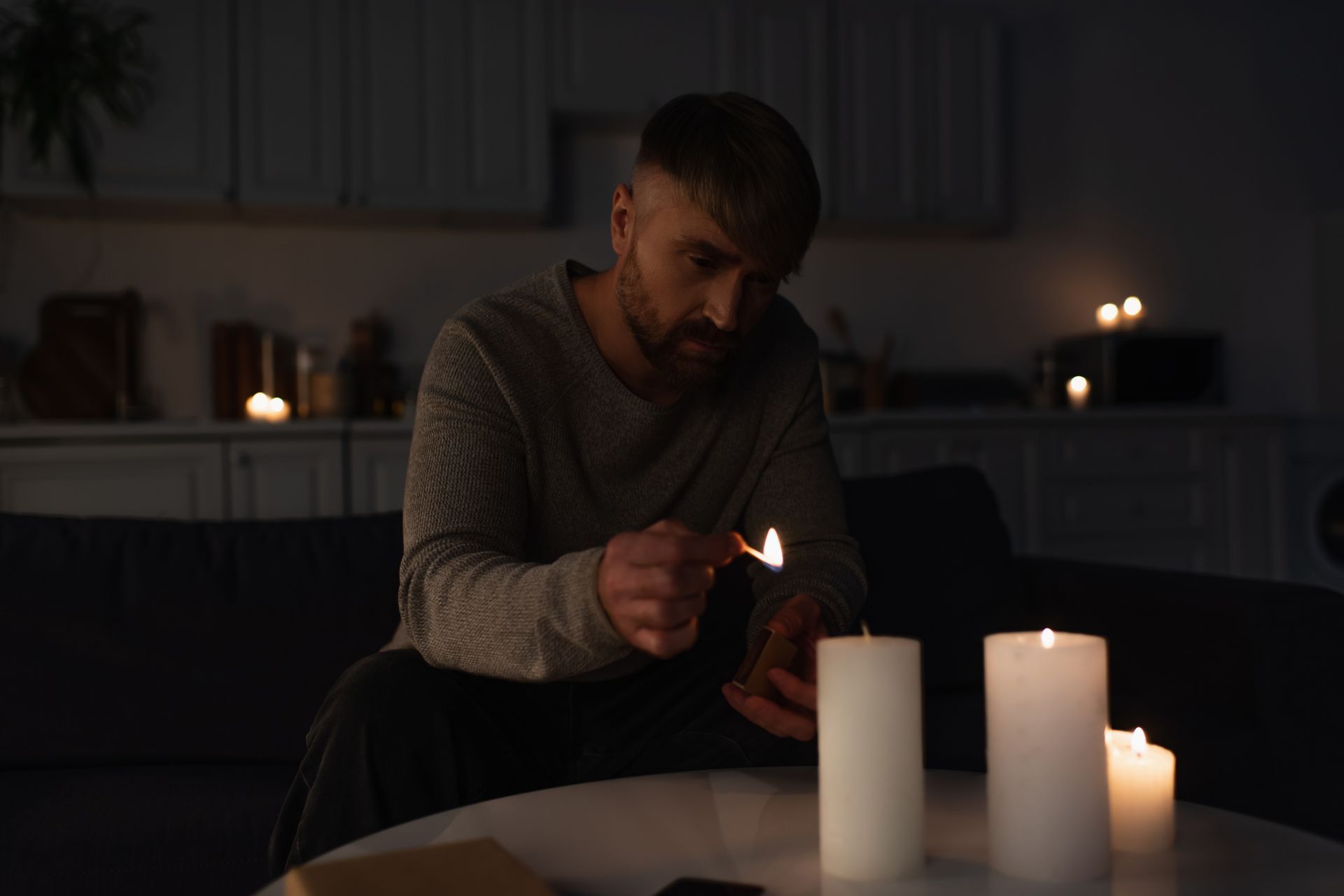 A man sitting in a dark room, lighting candles during a power outage in the area