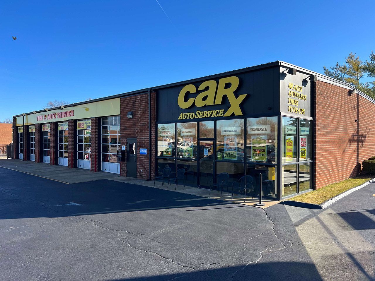 CarX Auto Service storefront with yellow and black signage, brick exterior, and sunny sky.