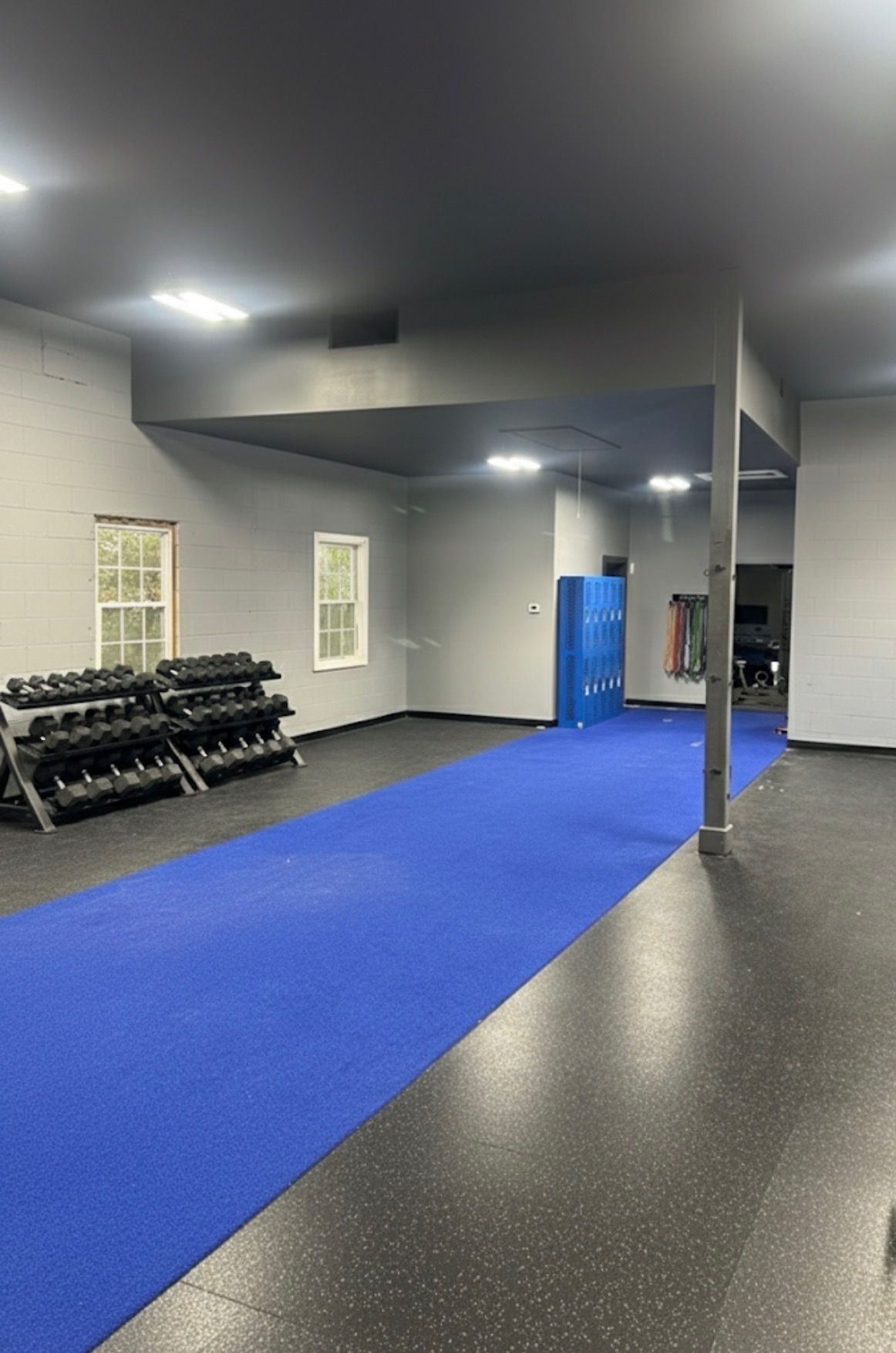 Gym interior with dumbbells, blue mat, and gray walls.