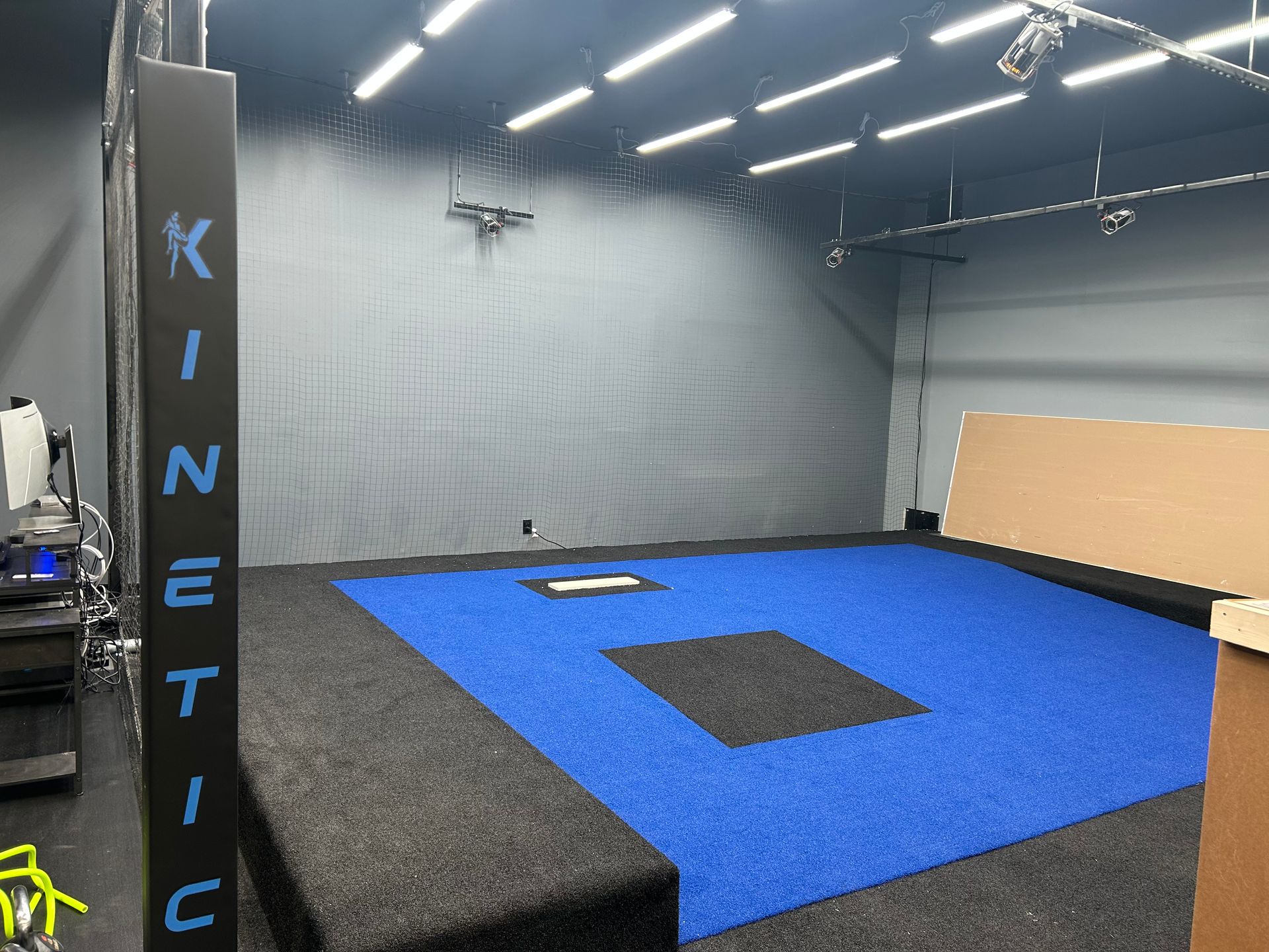 A batting cage with blue and black turf, gray walls, and 