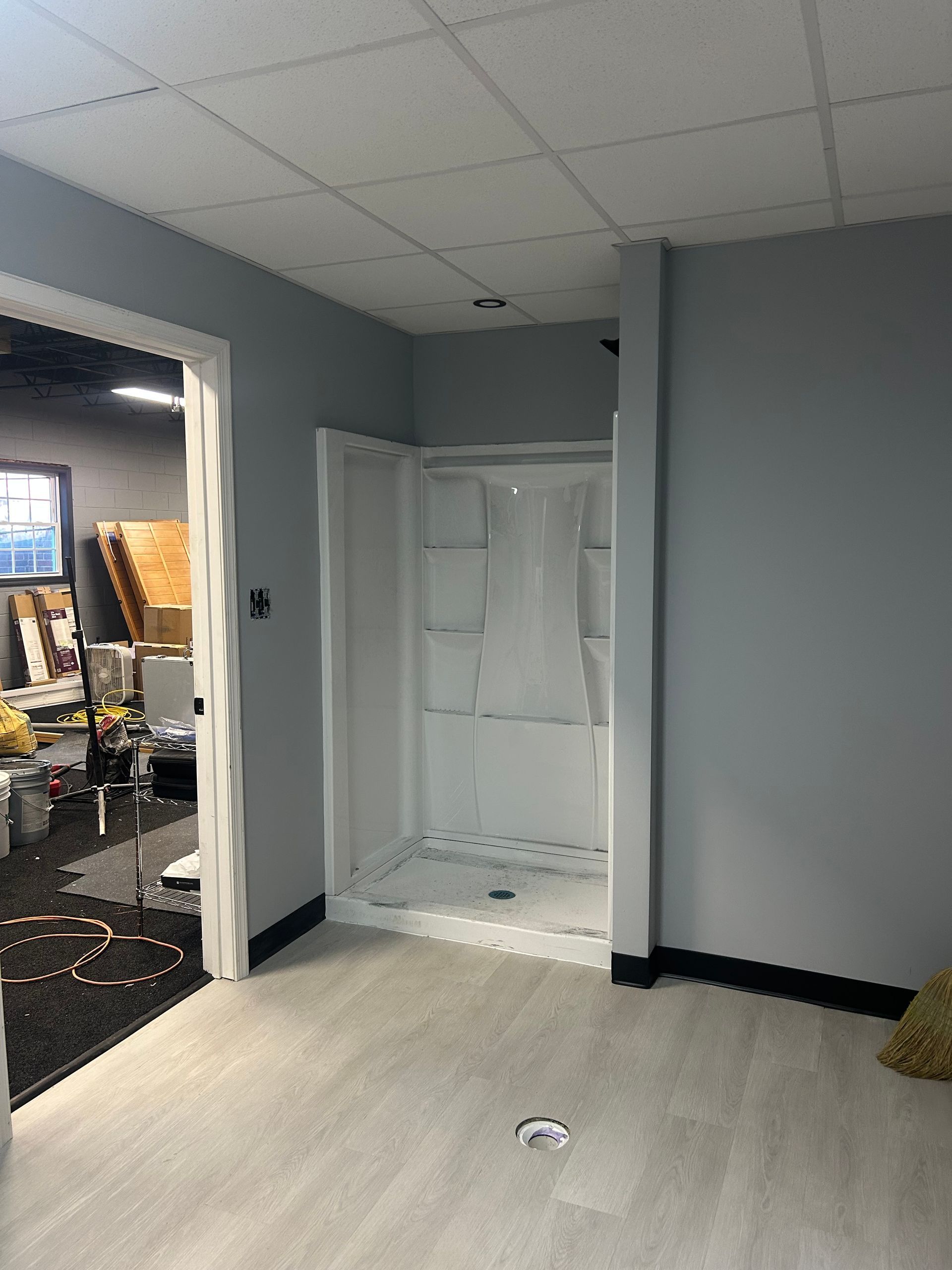 A small shower unit in a room with light gray walls and flooring. The shower has a white interior and a translucent shower curtain.