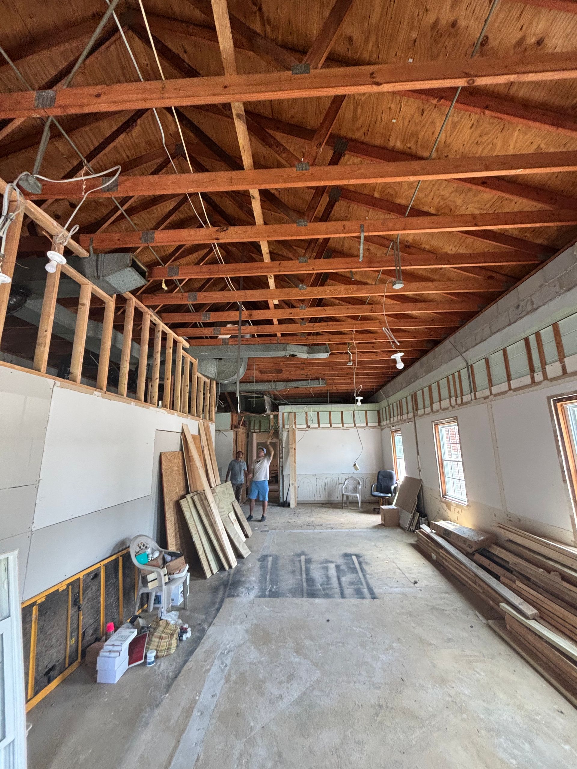 Interior of a building under renovation with exposed wooden beams, studs, and concrete floor. Two people stand in the center.